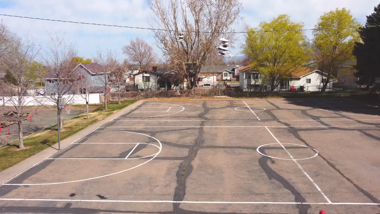 Slow pan drone clip sideways to the right of tennis shoes trainers on phone wire and a small and empty distressed basketball court after covid-19 lockdowns end
