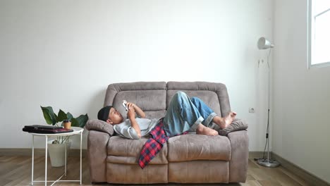 young asian college student in casual style using a smart phone lying on couch at home