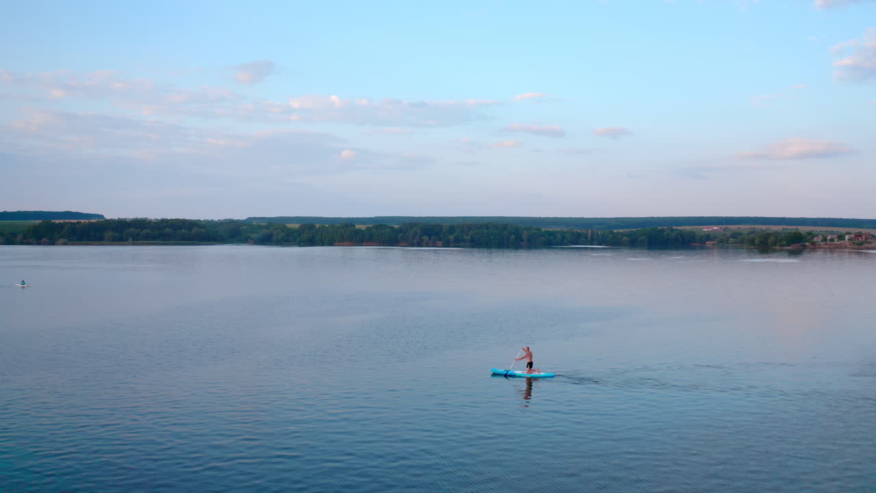 Active adventure on water. Sportsman training on water while standing on a board with oars on the background of beautiful summer landscape. Extreme sport concept