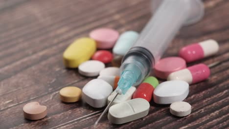 syringe and assorted pills on wooden surface