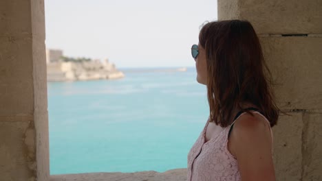 young woman looking out medieval city and sea coastline from stone window in three cities, malta