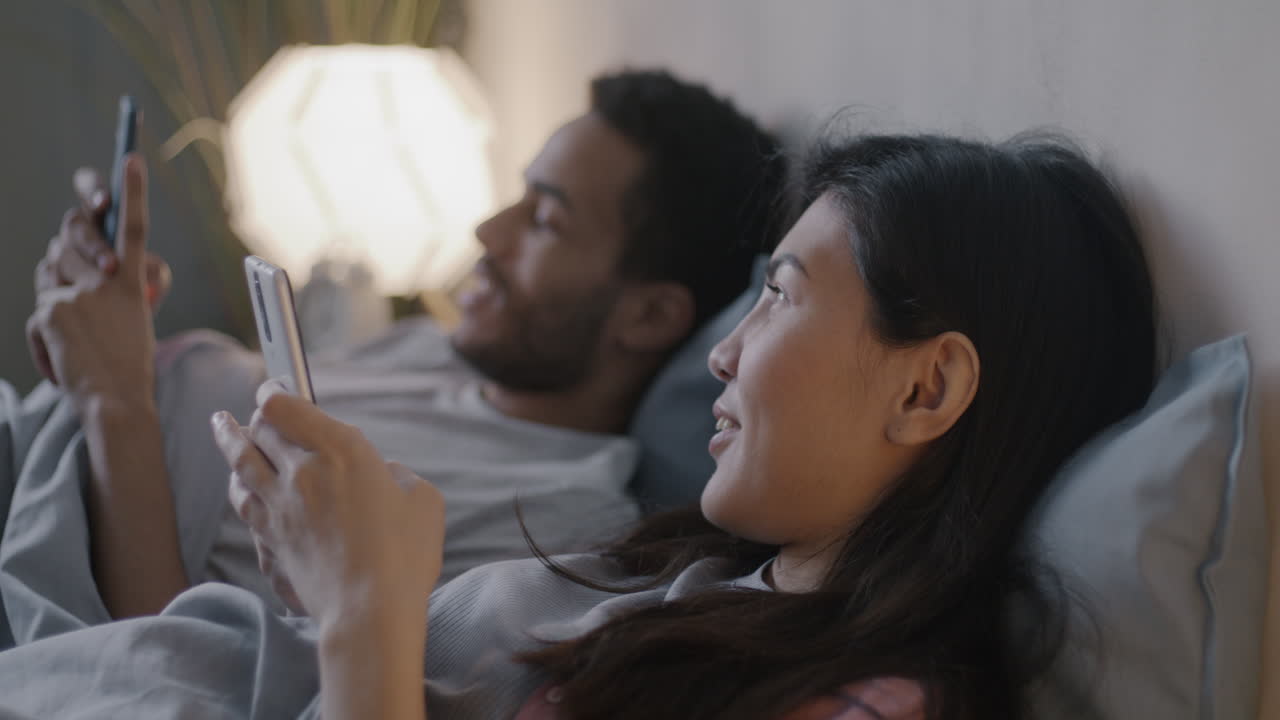 밤에 침대에서 스마트폰을 사용하는 커플
