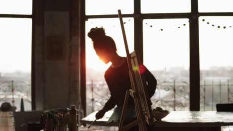 young cheerful female artist places canvas on easel and gets ready to start painting.