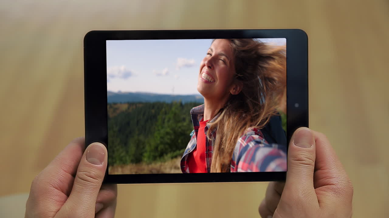 Primer plano de un hombre haciendo una videollamada con una tablet en casa. Un chico sostiene un ordenador digital mientras chatea