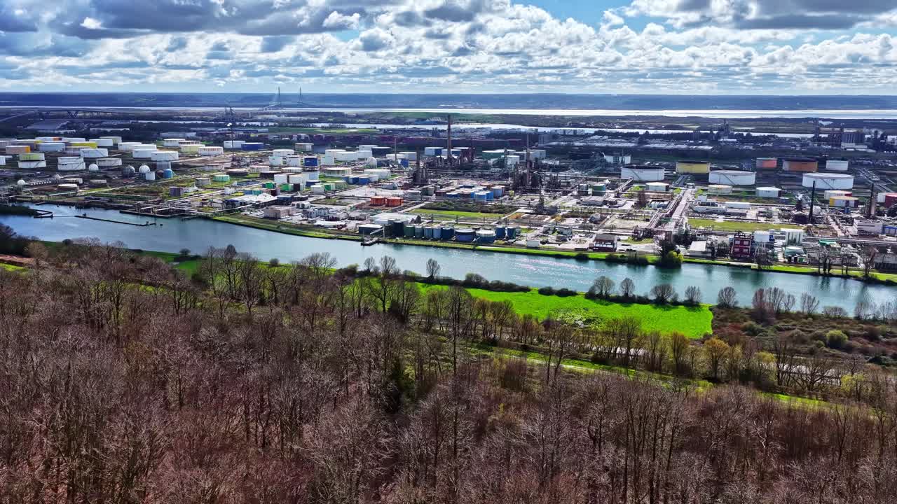 Udstrakt raffinaderi og industrihavnezone flankerer en bred kanal omkranset af nøgent forårsskovområde. Luftfoto af Havre, Frankrig.