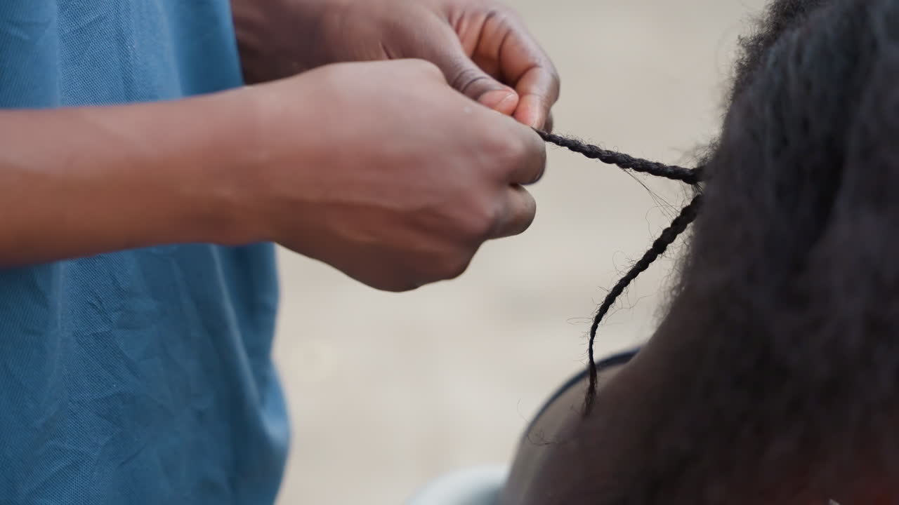 Scena di strada con attività di acconciatura. Un individuo fissa le punte delle trecce durante un vivace momento di strada cittadina. Una persona sistema attentamente i capelli in un'animata strada cittadina mentre altri osservano.