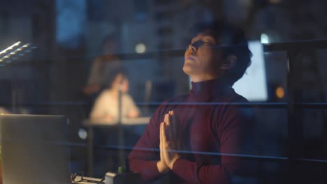 empresario asiático estresado meditando en postura de yoga en la oficina nocturna.