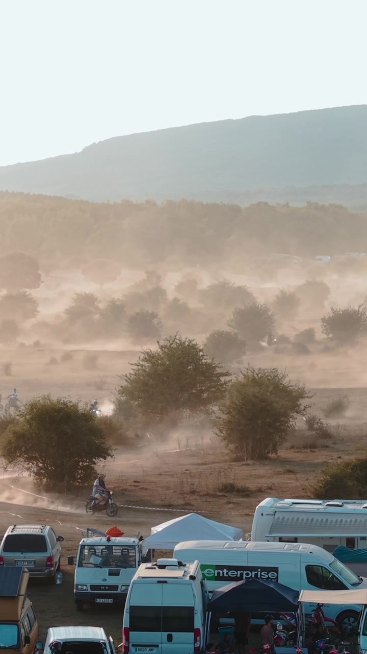 Piloti di motocross in gara attraverso un campo polveroso al tramonto