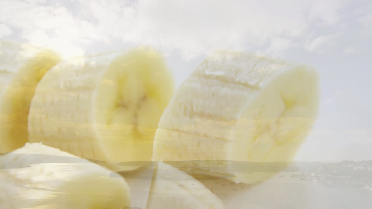 Animation of sliced banana pieces floating over serene landscape with cloudy sky