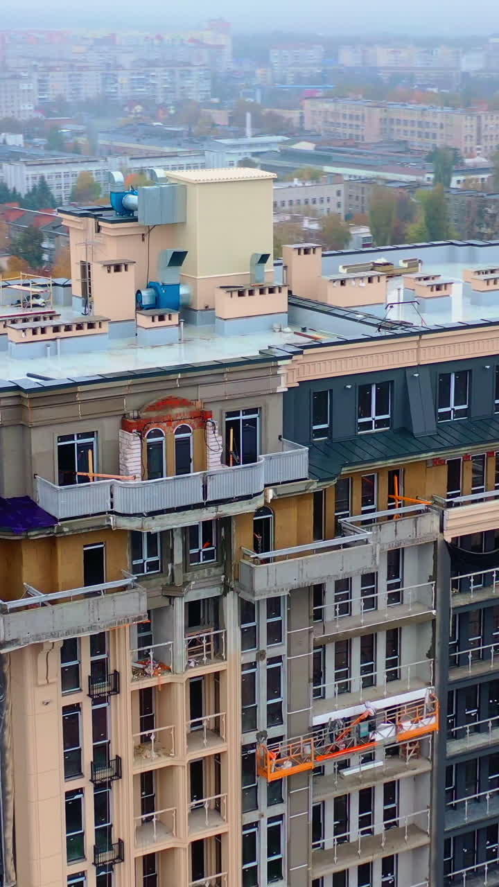 Construction site in the city. Modern architecture is building by workers. High-rise building under construction. Camera moves in a round way. Aerial view. Vertical video