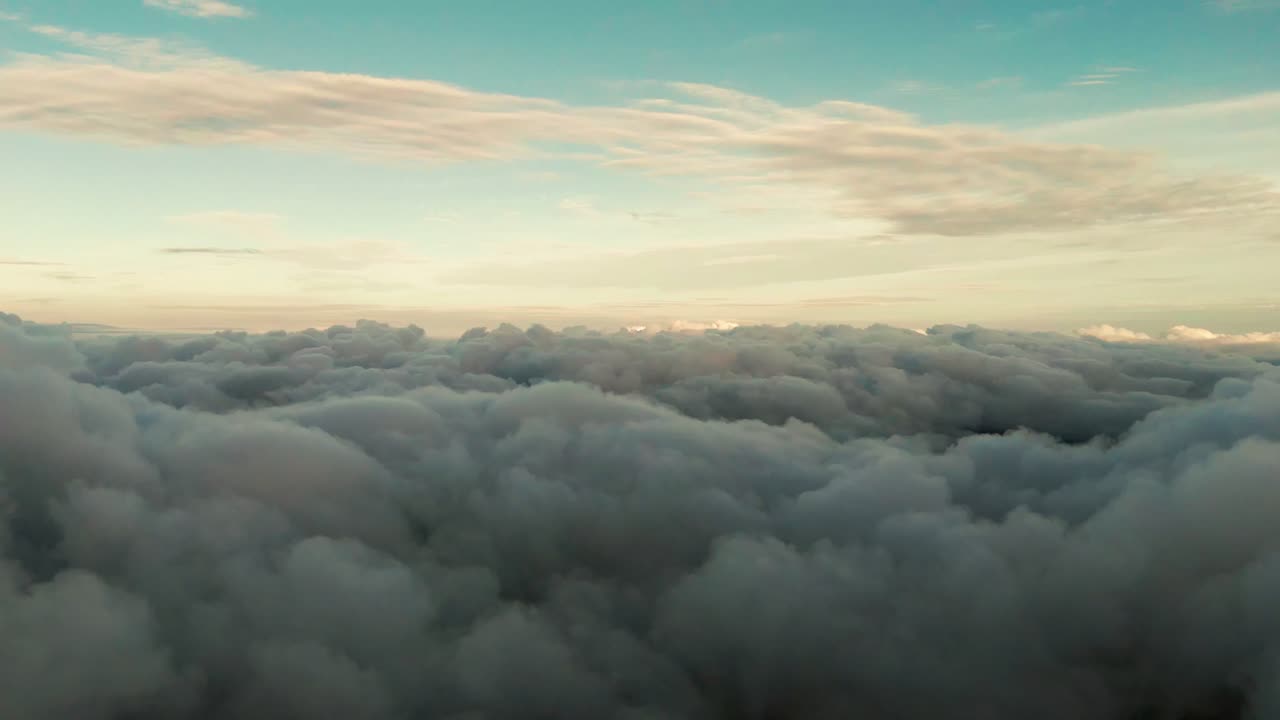 Ampia veduta aerea sopra fitte nuvole ondulate con calda luce dorata all'orizzonte e cielo azzurro tenue, un tranquillo paesaggio nuvoloso ad alta quota ideale per sfondi di viaggio da sogno e naturali.