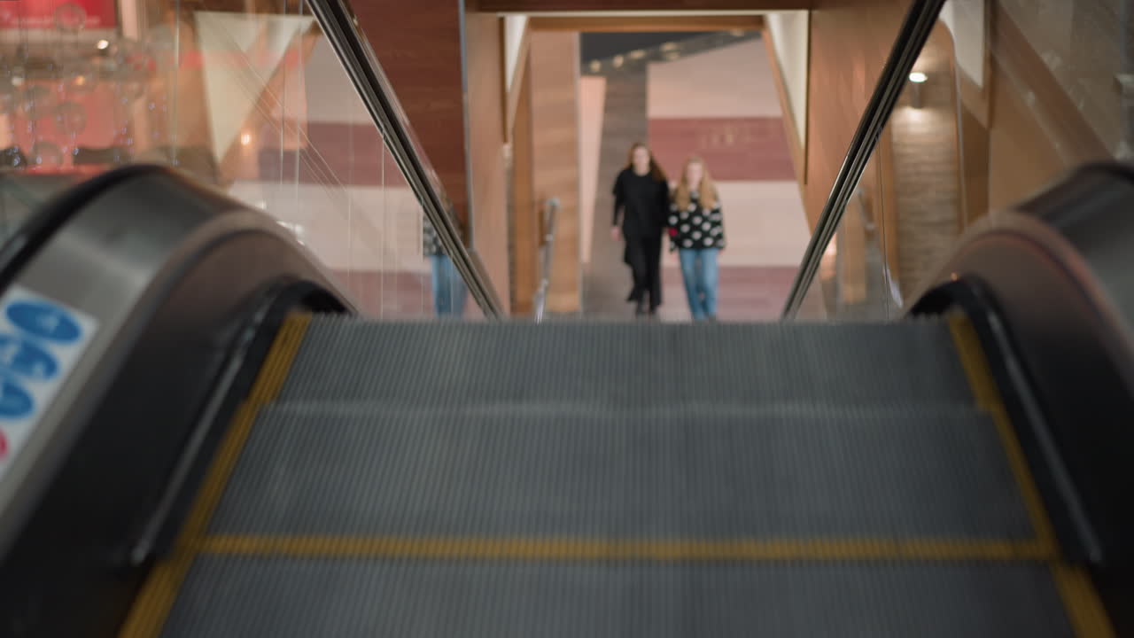 moving escalator ascending through glass in busy mall, shoppers approach from ground level, blurred figures convey motion, metallic steps with yellow safety edges and sleek handrails