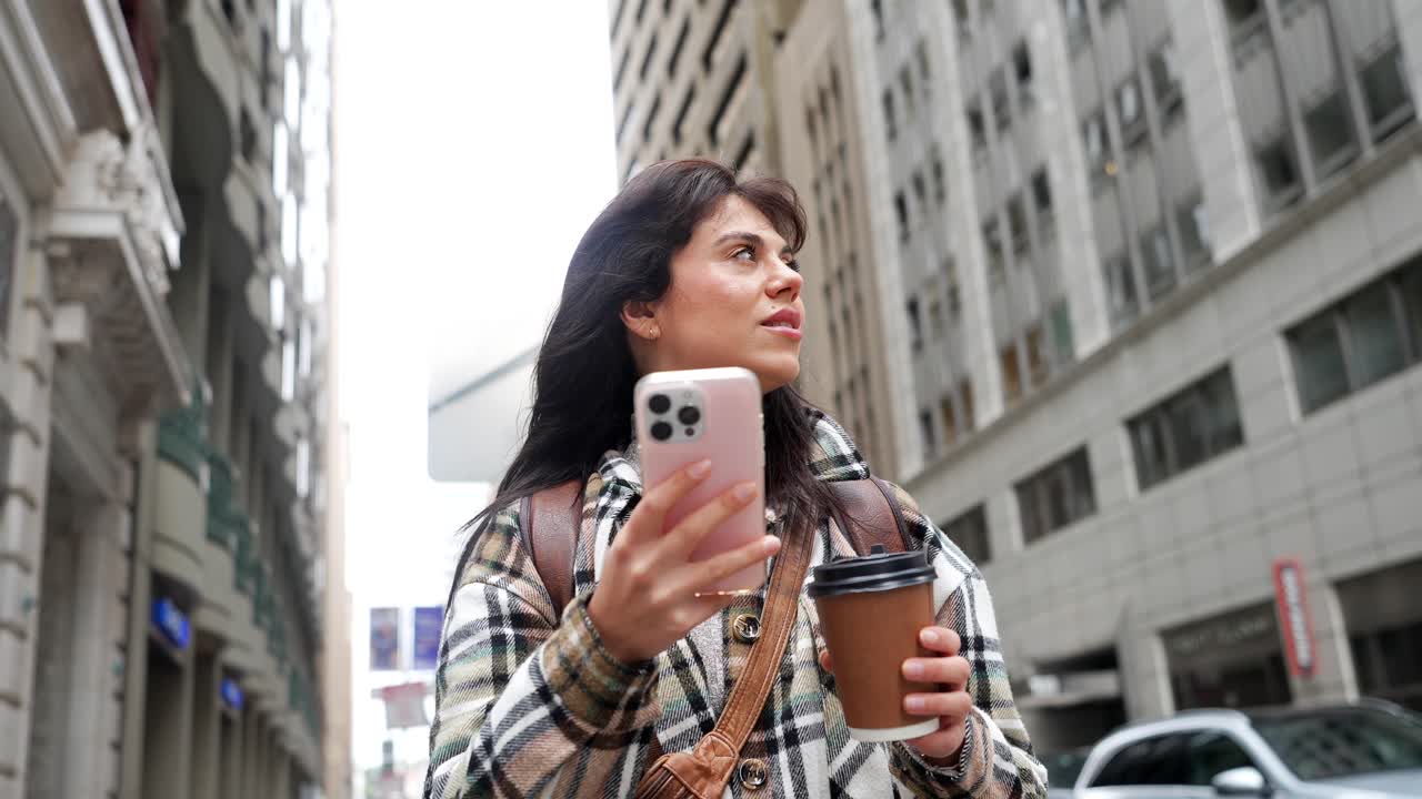 Giovane donna che usa lo smartphone e beve caffè per strada.