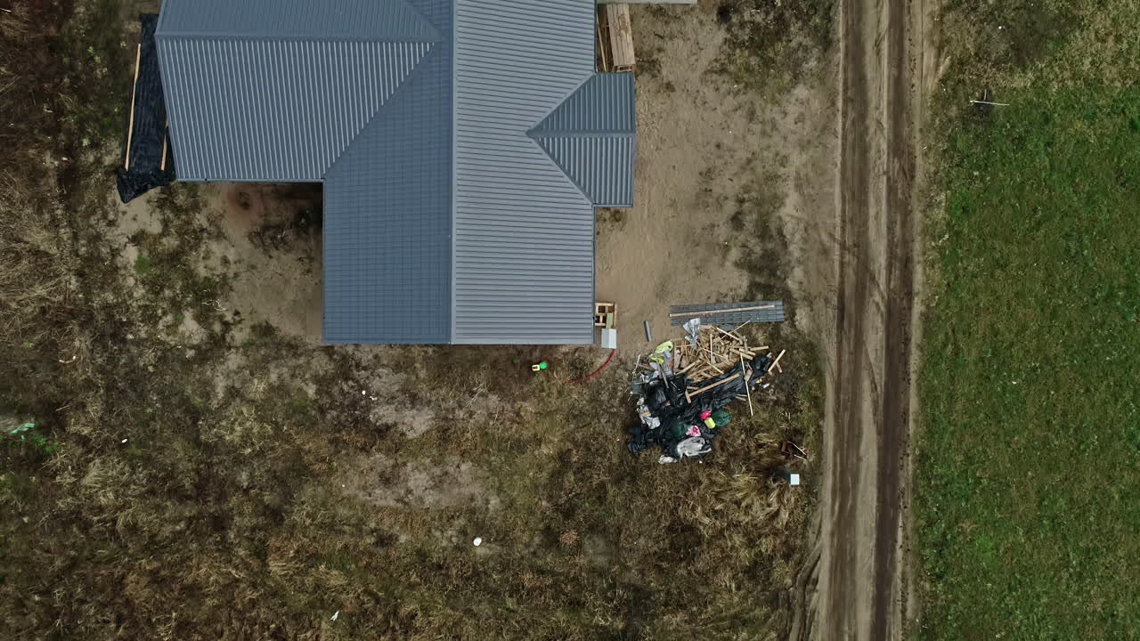 Landligt husmandssted med bølgebliktag, tilstødende grusvej, droneoptagelse på en klar dag