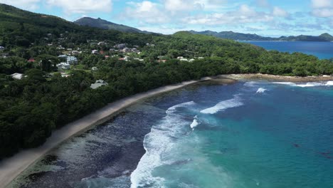 aerial view of a coastal mahe island landscape featuring lush greenery, pristine beaches, and distant mountains under a clear blue sky with scattered clouds.
