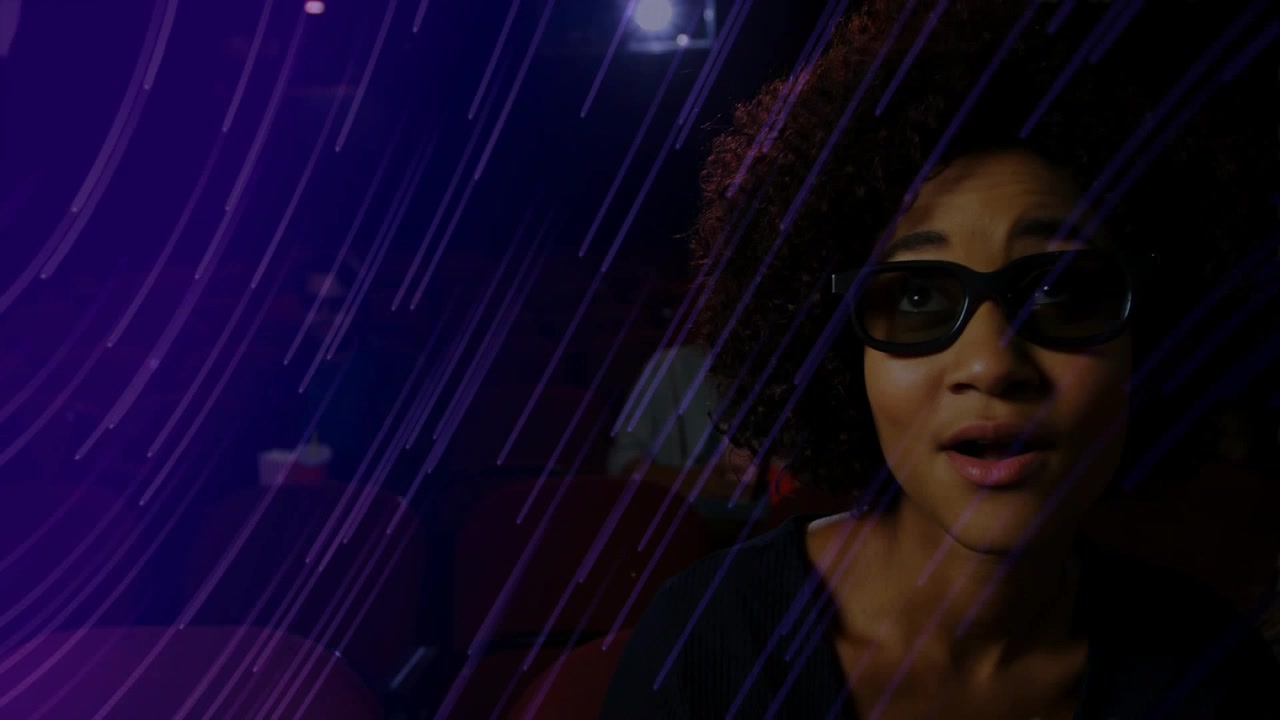 Donna con occhiali 3D seduta in un cinema illuminato di viola, proiettore che scorre, suscitando reazioni.