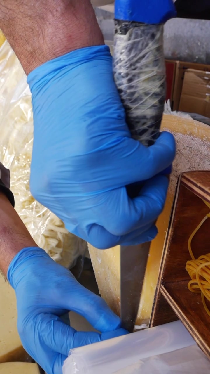 Formaggiaio che taglia una grande forma di formaggio stagionato