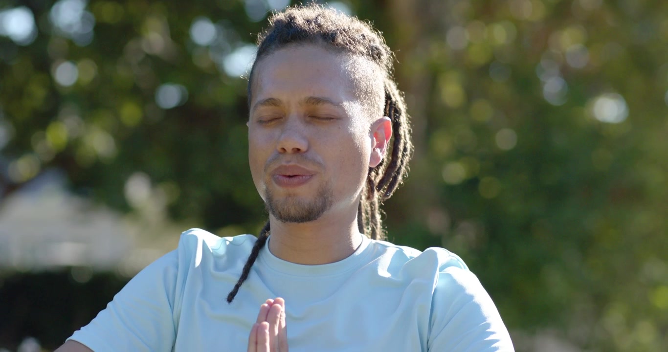 Uomo adulto afroamericano che inspira, alzando le braccia in preghiera per la calma, indossando un orologio al parco.