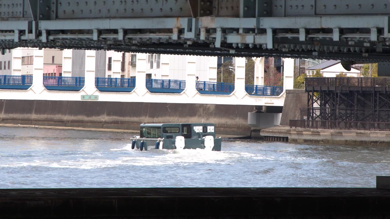 Ponte industriale in acciaio che incornicia un piccolo battello per pendolari che naviga sul fiume Sumida a Tokyo.