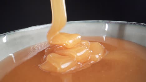 macro shot of delicious honey pouring into a bowl with a black background