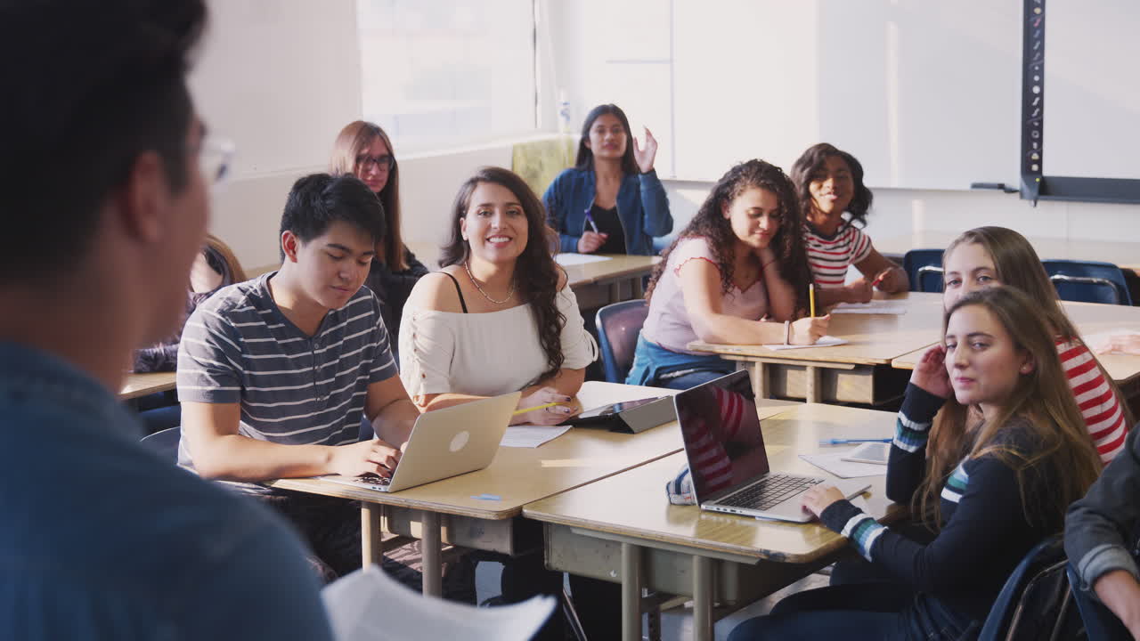 vista trasera de un maestro de secundaria de pie frente a la clase enseñando una lección