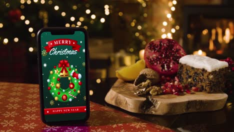 teléfono móvil con mensaje de feliz navidad con árbol de comida festiva y regalos en el fondo