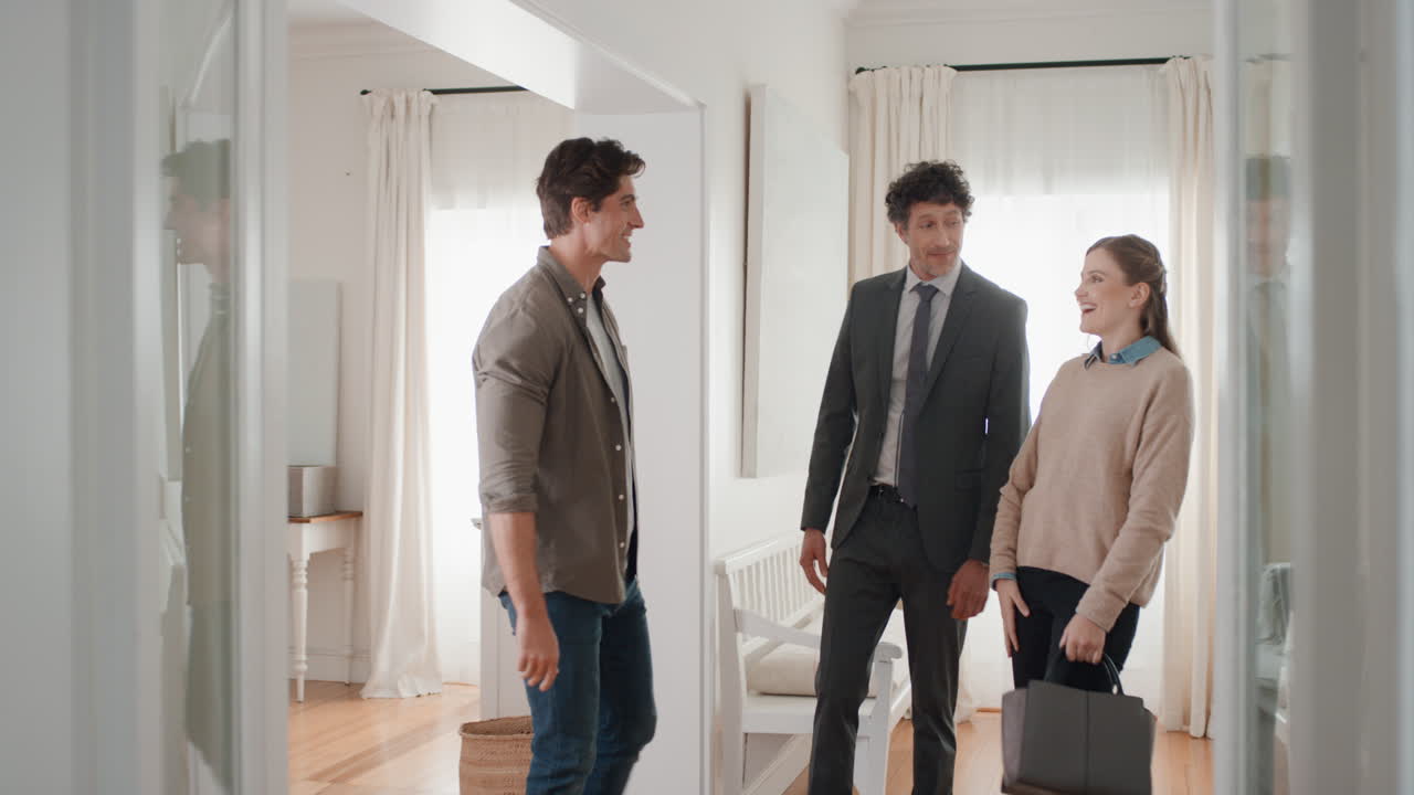 부동산 에이전트가 젊은 부부에게 새로운 집을 보여주고 부동산 투자를 제시합니다. 행복한 고객들이 부동산 에이전트와 손을 흔들고 성공적으로 집을 구입합니다. 4k 영상
