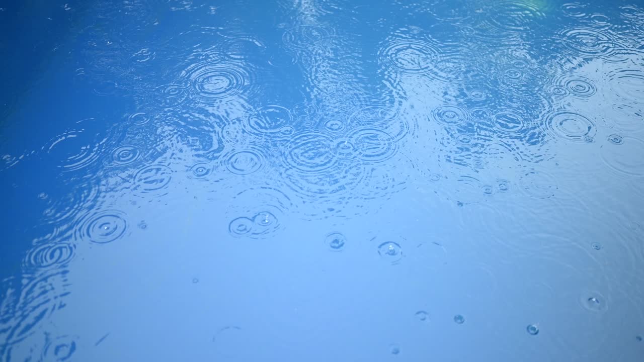 파란 물의 표면에 비방울의 원. 추상적인 배경. 수영장에서의 비.