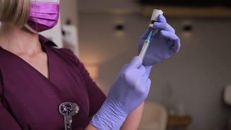 The nurse, wearing a purple mask and gloves, is preparing a vaccine with careful gestures using her fingers and thumbs