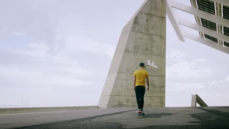 Young-Attractive-Trendy-Man-skateboarding-fast-under-a-solar-panel-on-a-morning-sunny-day-with-an-urban-city-background-in-slow-motion