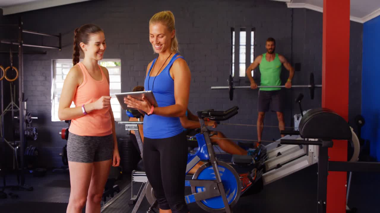 디지털 태블릿을 사용하는 동안 여성 트레이너가 여성과 상호 작용합니다.