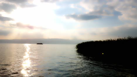 Silhouette-of-a-ship-moving-on-a-calm-lake-toward-cane-and-reed