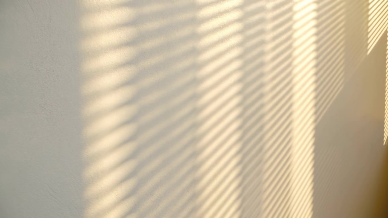 Bright minimalist room corner with sunlight casting diagonal shadows across a plain wall beside a window shutter, creating a calm warm atmosphere and subtle