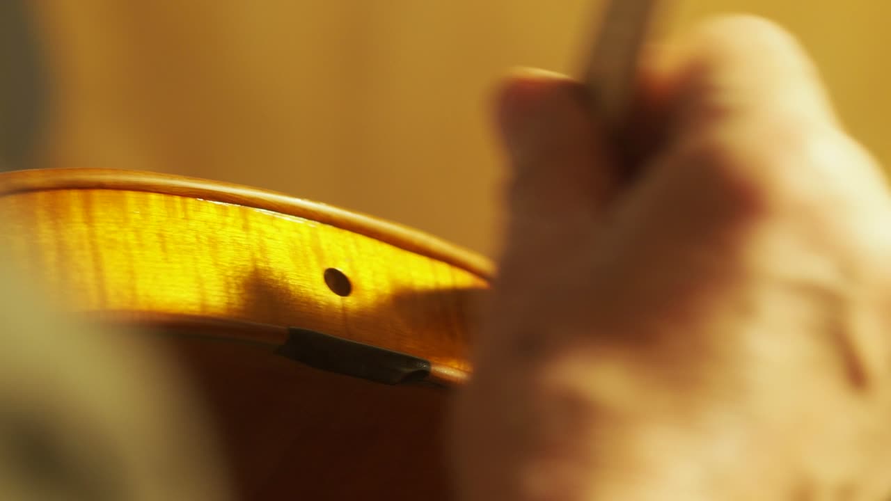 mano de un luthier fabricante de violines barnizando un instrumento de cuerda de madera hecho a mano