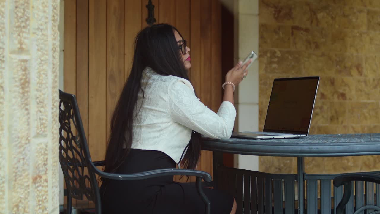 A woman in business clothes engrossed in her laptop at an open-air office.
