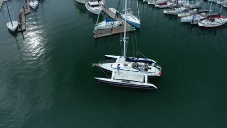 un catamarán entra lentamente en los amarres en el día de la nube del puerto deportivo