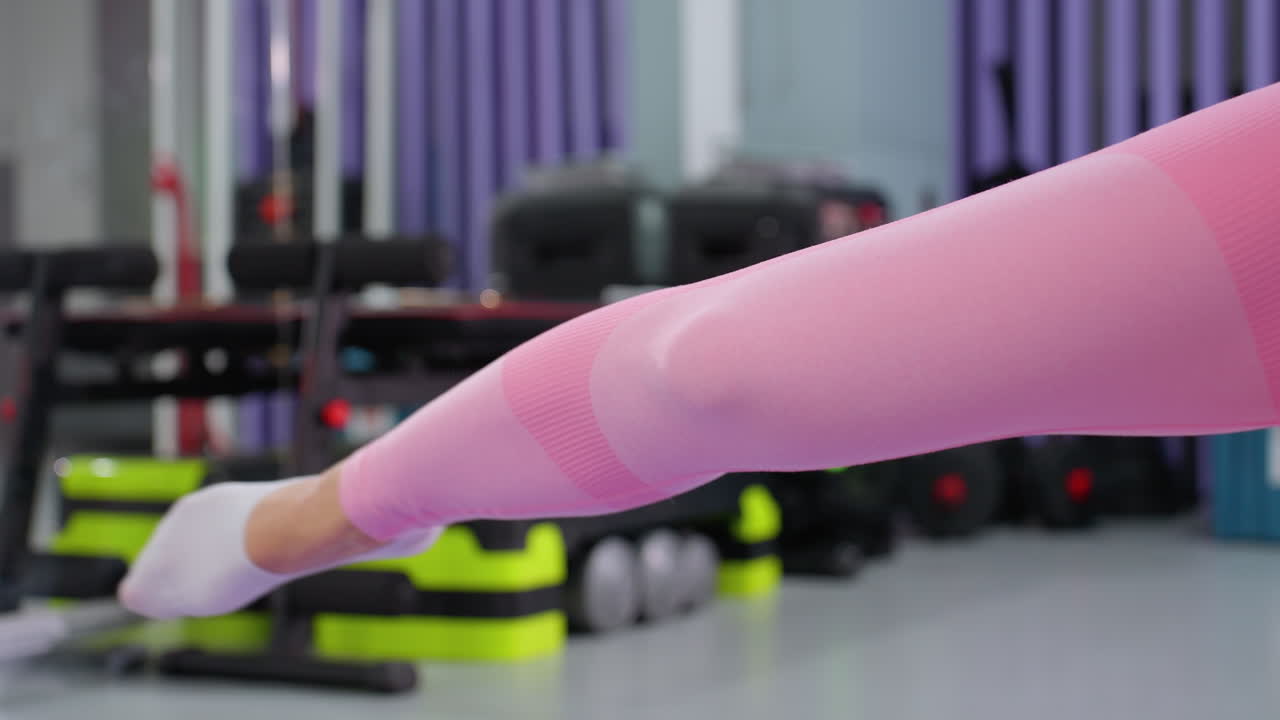 primer plano de estiramiento de las piernas durante el entrenamiento en el gimnasio, el fondo presenta varios equipos de fitness, incluida una caja de música que emite luces de colores parpadeantes