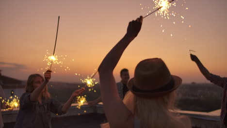 Young-russian-people-raise-their-hands-up-and-jump-on-the-roof-with-big-bengal-light-in-their-hands.-It's-a-crazy-party-at-night.