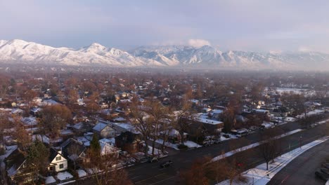 Drohnen-Dolly-über-Einer-Großen-Ausfallstraße-Und-Vororten-Mit-Schneebedeckten-Wasatch-Bergkämmen