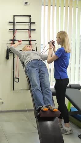in a gym a woman helps a man exercise while another rests nearby in a serene gym a woman assists a man with exercises on a bench ensuring proper form nearby another woman rests showcasing companionships role in wellness