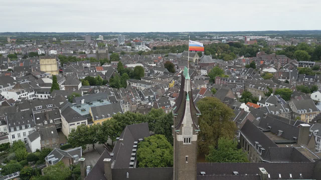 Drone shot of a church tower with Dutch flag above the historic city of Maastricht
