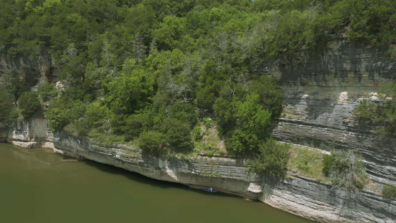 человек в синем каяке гребёт рядом с скалистым скалом, исследуя спокойный водный путь в тени