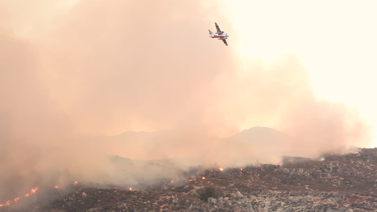 avión de bomberos volando sobre humo gris, saliendo de un incendio forestal