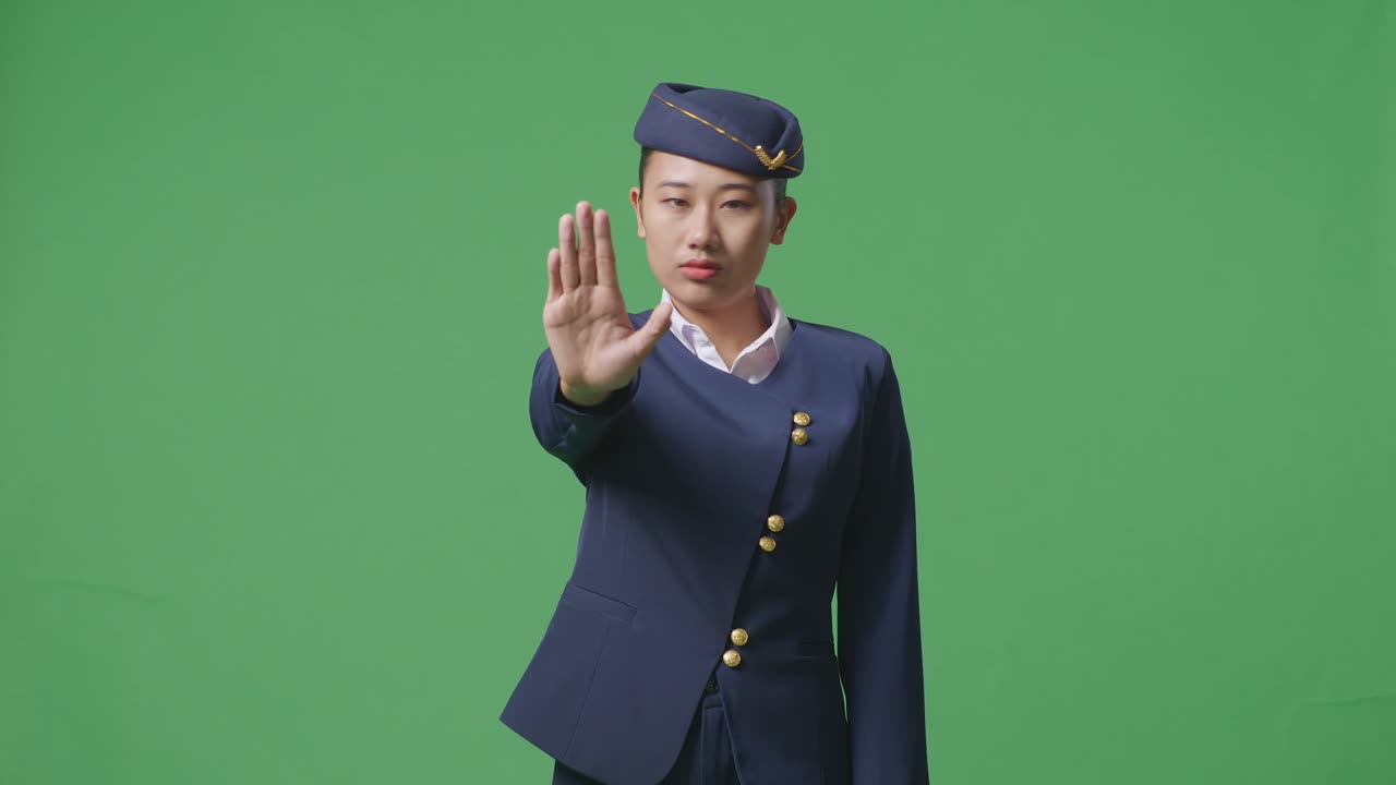 Donna asiatica assistente di volo che guarda in camera e disapprova con un gesto della mano di negazione, su sfondo green screen in studio.