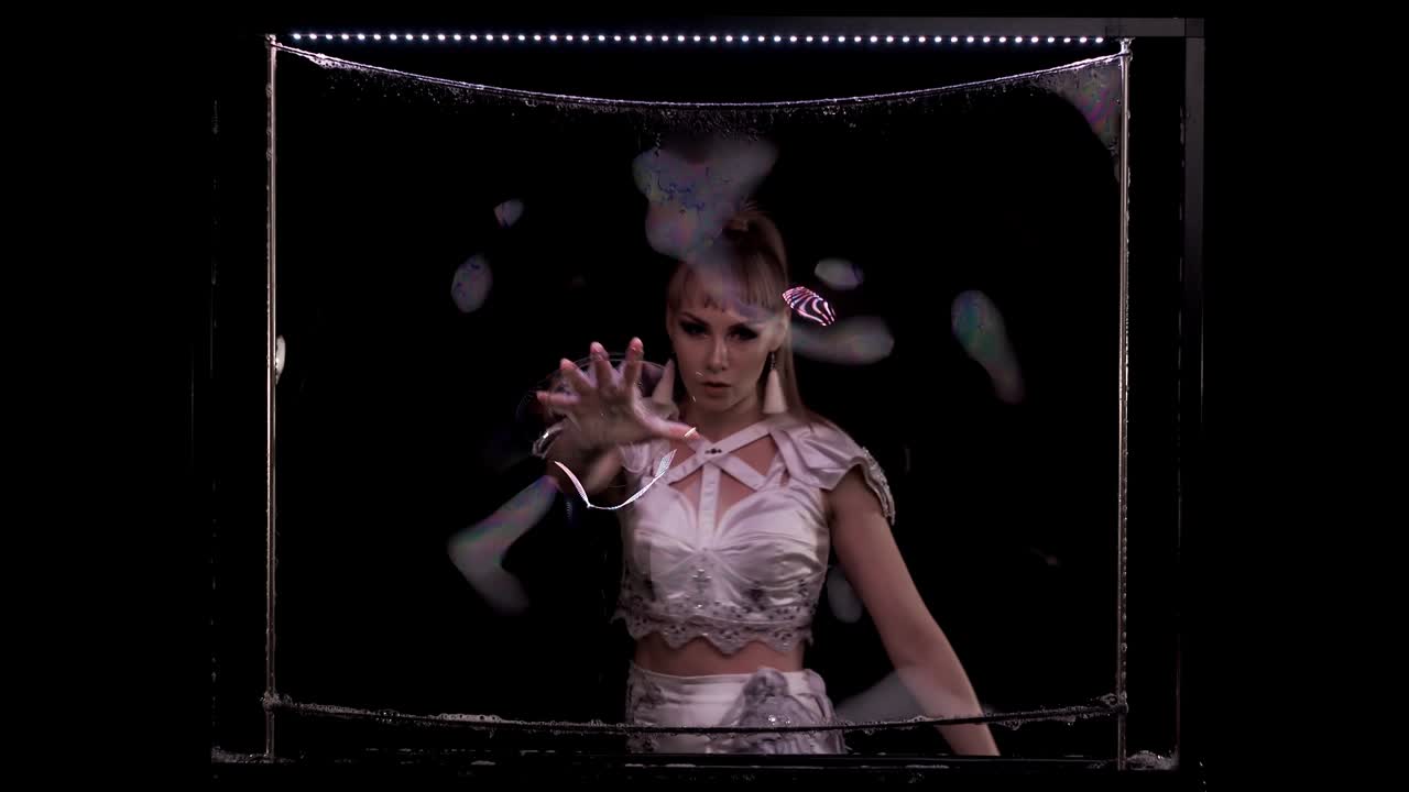 девушка делает трюки с мыльными пузырьками. она играет с рукой на мыльном экране на вертикальной раме с светодиодным светом