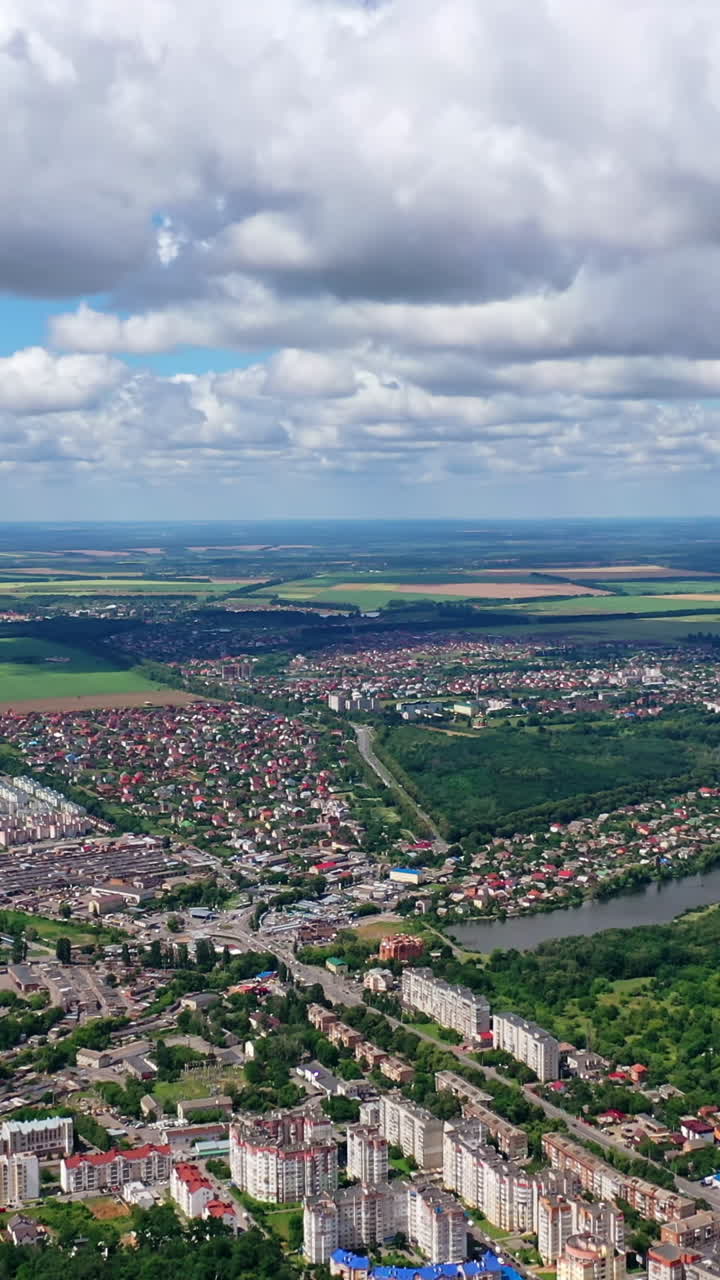City landscape in summer. River flowing in the city. View from above on the city on the beautiful nature background. Aerial view. Vertical video