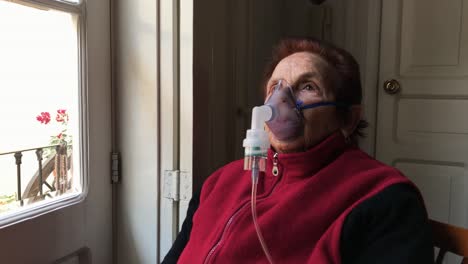 caucasian elderly woman inhaling medication mist from nebulizer treatment by a window at home