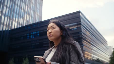 Low-angle-view-of-business-Chinese-woman-walking-in-the-city-and-using-phone