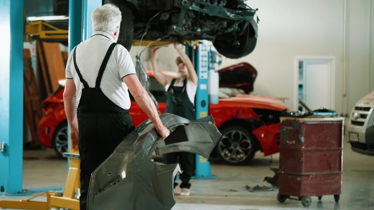 el viejo mecánico trae un parachoques nuevo para comprobar si encaja en el coche dañado en el taller.
