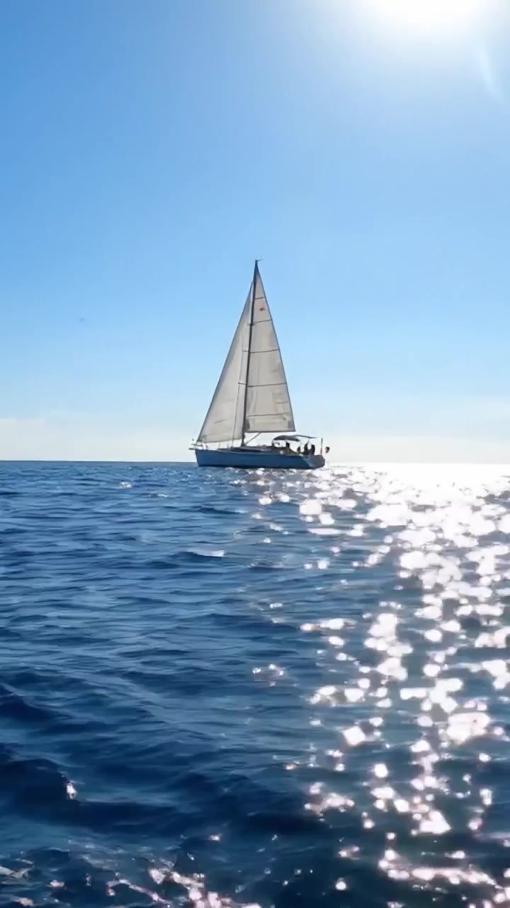 Un impresionante velero deslizándose sobre aguas tranquilas bajo un cielo azul claro, rodeado de brillantes reflejos de la luz del sol